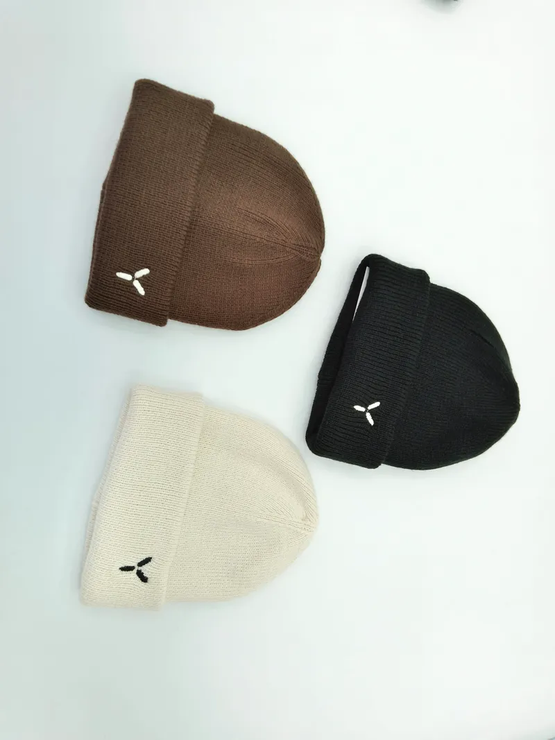 Drei gefaltete Umschlag-Beanies in Schokobraun, Schwarz und Naturweiß mit kleinem eingesticktem Logo auf hellem Untergrund