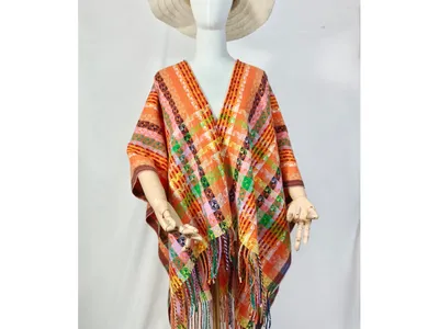 Weiße Schaufensterpuppe mit orangefarbenem handgewebten geometrischen Poncho mit Fransensaum und naturfarbenem Breitkrempen-Hut