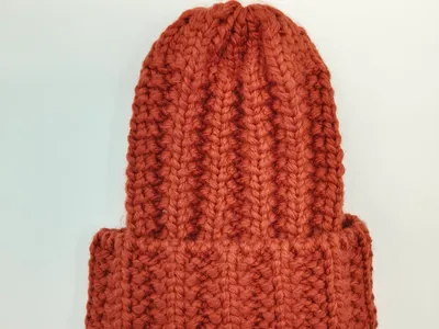 Rostfarbene Grobstrick-Mütze mit Umschlagrand und handgestrickter Wolltextur flach auf weißem Hintergrund liegend