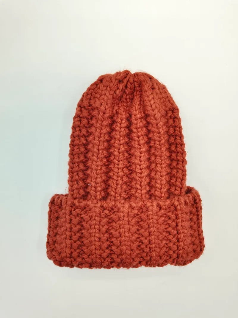 Rostfarbene Grobstrick-Mütze mit Umschlagrand und handgestrickter Wolltextur flach auf weißem Hintergrund liegend