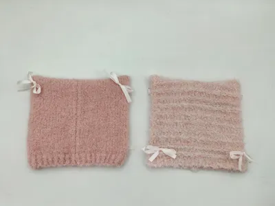 Zwei altrosafarbene flauschige Strickstulpen mit weißen Satinschleifen in Nahaufnahme auf weißem Hintergrund