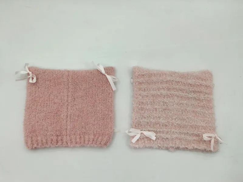 Zwei altrosafarbene flauschige Strickstulpen mit weißen Satinschleifen in Nahaufnahme auf weißem Hintergrund