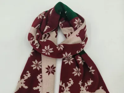 Weinroter und cremefarbener Strickschal mit nordischem Rentier- und Schneeflockendesign, drapiert auf weißem Hintergrund