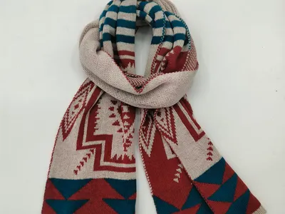 Gefalteter Strickschal mit geometrischem Südwest-Muster in Creme, Rostrot und Petrolblau auf weißem Hintergrund