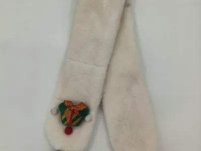 Cremefarbener Kunstfell-Schal mit grünen und roten Wollbommeln und bestickter Weihnachtsglocken-Brosche auf weißem Hintergrund