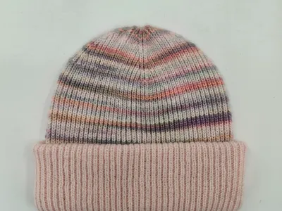 Flauschige Wintermütze mit bunten Streifen in Rosa, Lila und Grau sowie breitem gestricktem Umschlagrand auf weißem Untergrund