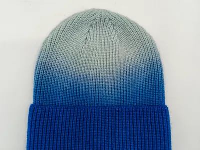 Strukturierte Wintermütze mit markanter Farbverlauf-Optik von Taubenblau zu Grau, flach aufgenommen auf hellem Hintergrund