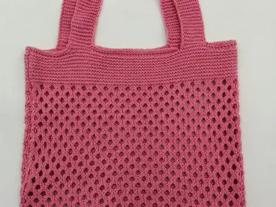 Handgefertigte Einkaufstasche aus rosa Baumwollgarn mit durchbrochenem Häkelmuster und zwei festen Henkeln auf weißem Hintergrund