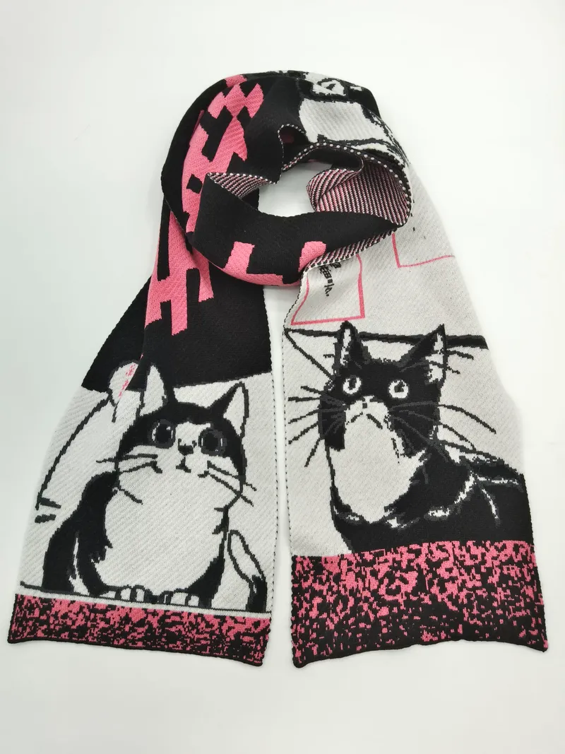 Gestrickter Schal mit schwarz-weißen Smoking-Katzen-Illustrationen und pinkfarbenen geometrischen Akzenten, aufgerollt auf hellem Hintergrund