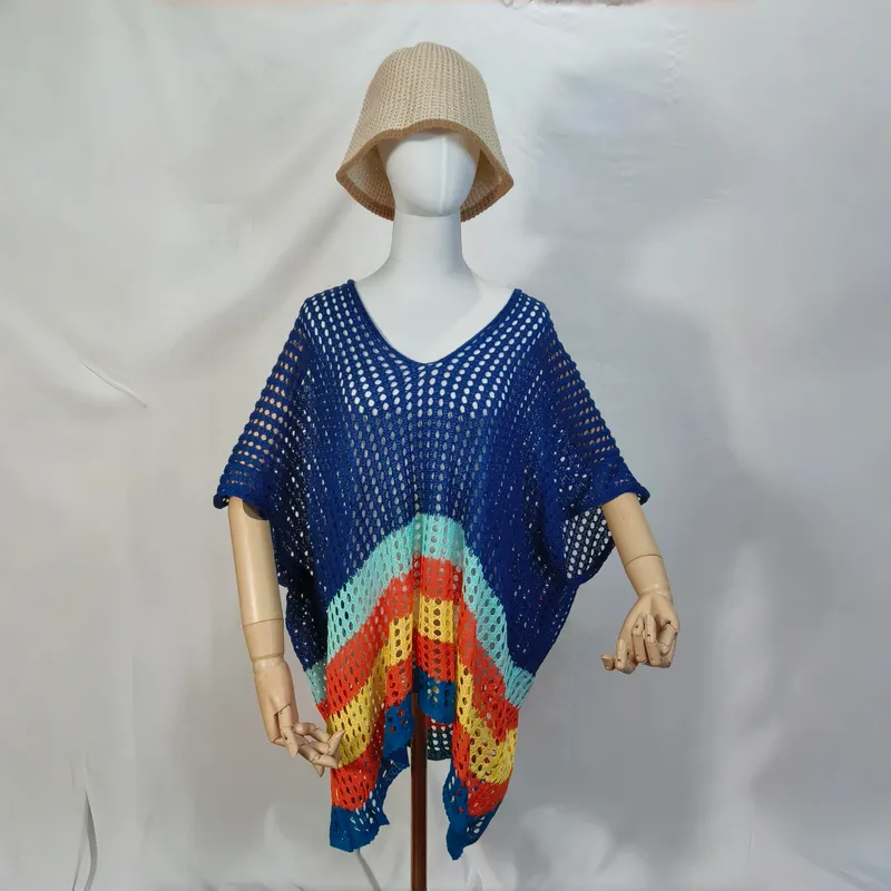Blaue offene Häkelweste als Poncho mit buntem Streifenabschluss und beigefarbenem Bucket Hat vor weißem Hintergrund
