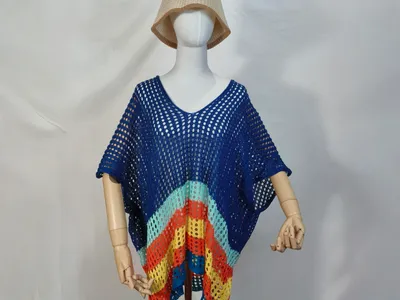 Blaue offene Häkelweste als Poncho mit buntem Streifenabschluss und beigefarbenem Bucket Hat vor weißem Hintergrund