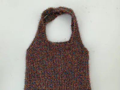 Handgestrickte flauschige Tragetasche aus buntem Garn in Braun, Blau und Rosa mit einfachem Schlaufengriff auf weißem Hintergrund
