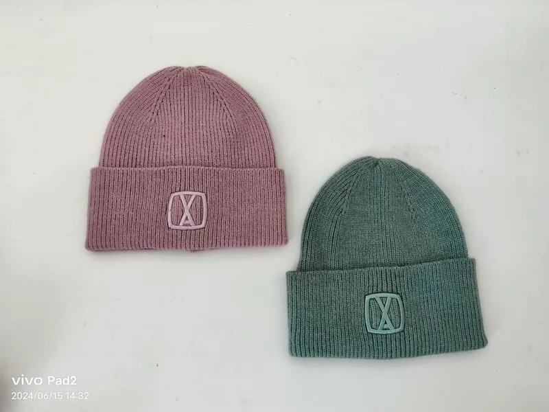 Zwei gefaltete Rippenstrickmützen in altrosa und salbeigrün mit dezenter Logostickerei, Draufsicht auf hellem Untergrund