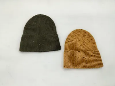 Zwei Rippenstrickmützen mit bunten Garneinschlüssen in Olivgrün und Senfgelb, nebeneinander auf weißem Hintergrund