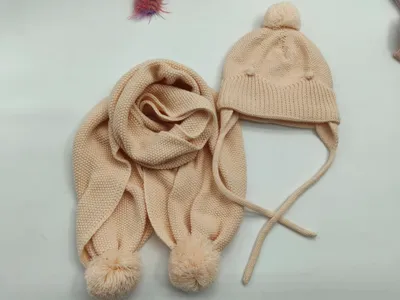 Kinderwintersset aus cremefarbenem Strick: Ohrenklappenmütze mit Bommel oben sowie passender Schal mit Bommelenden