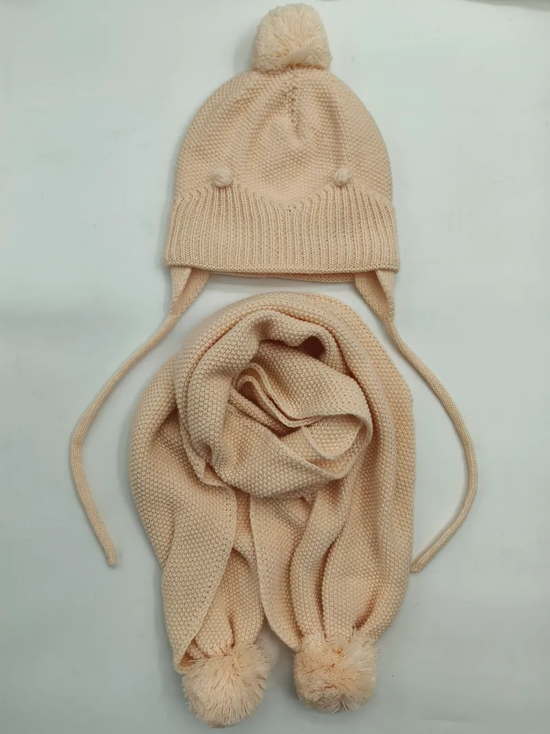 Cremefarbenes Kinderstrick-Set: Beanie mit Pompon und Ohrenschutz sowie zugehöriger Strickschal mit Pomponenden