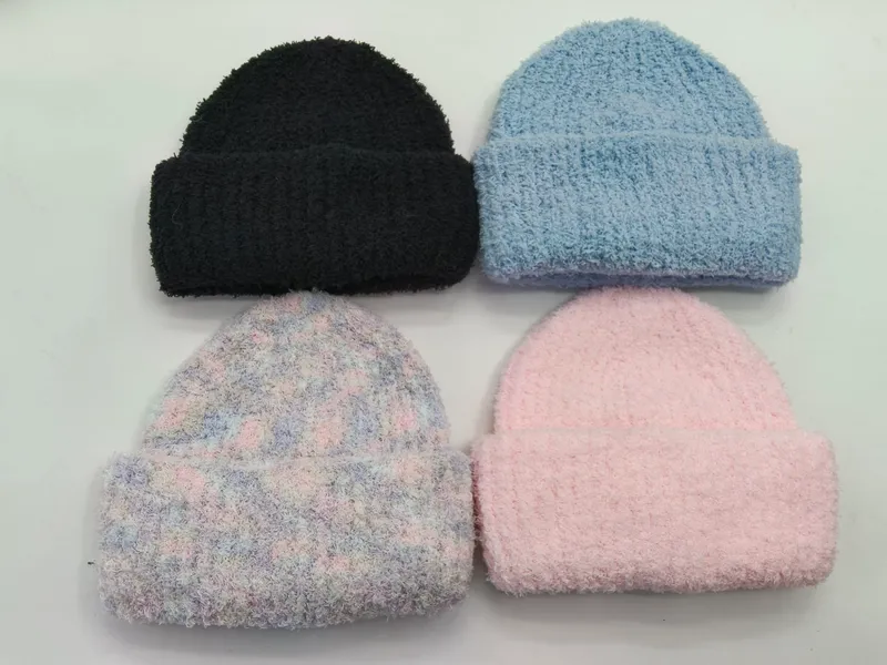 Vier pelzige Strickmützen flach liegend in Schwarz, Hellblau, Pastellbatik und zartem Rosa auf weißem Hintergrund
