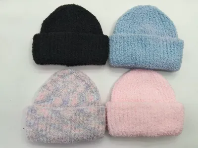 Vier flauschige Umschlag-Beanies in Schwarz, Hellblau, Pastellbatik und Rosa, flach auf weißem Hintergrund liegend