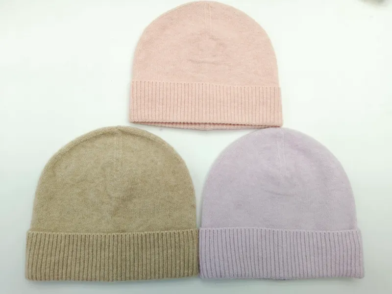 Drei Strickmützen mit Rippenbündchen in Altrosa, Sandbeige und Lavendel, flach auf weißem Untergrund angeordnet