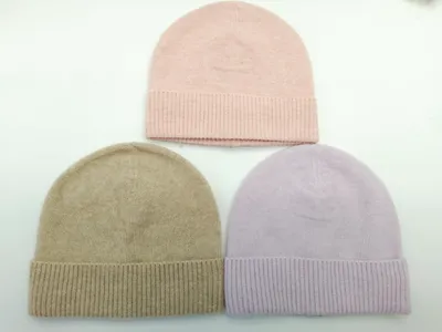 Drei Strickmützen mit Rippenbündchen in Altrosa, Sandbeige und Lavendel, flach auf weißem Untergrund angeordnet