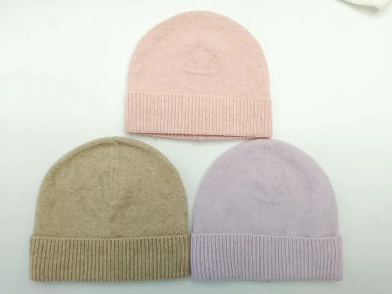 Drei gefaltete Rippenbündchen-Beanies in Altrosa, Taupe und Lavendel flach auf weißer Fläche liegend
