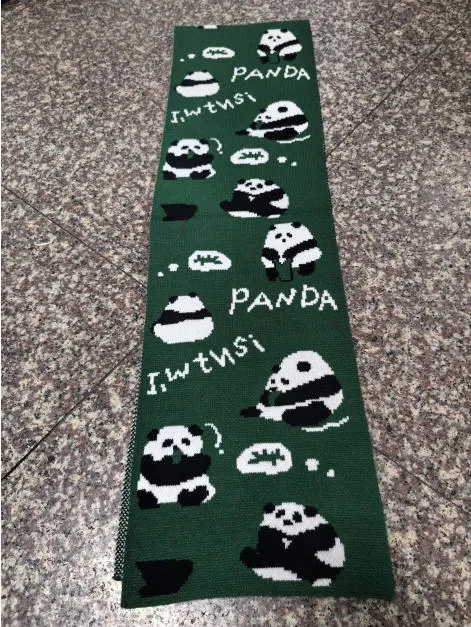 Dunkelgrüner Wollschal mit gestrickten Panda-Illustrationen und PANDA-Schriftzug, flach auf Fliesenboden liegend
