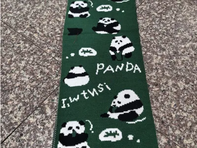 Dunkelgrüner Wollschal mit gestrickten Panda-Illustrationen und PANDA-Schriftzug, flach auf Fliesenboden liegend