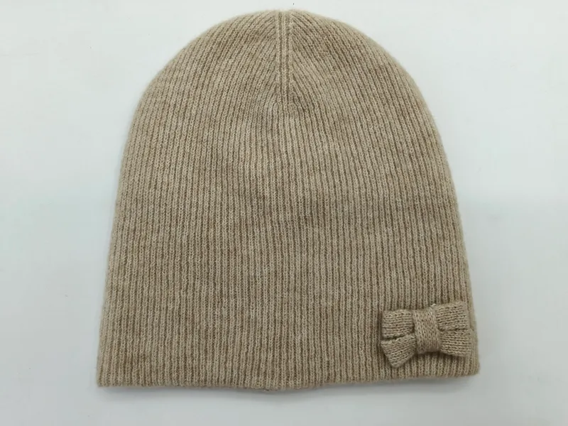 Hellbeige Strickmütze mit feiner Rippentextur und kleiner dekorativer Schleife an der Seite, Draufsicht auf weißem Untergrund
