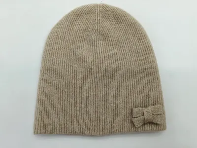 Hellbeige Strickmütze mit feiner Rippentextur und kleiner dekorativer Schleife an der Seite, Draufsicht auf weißem Untergrund