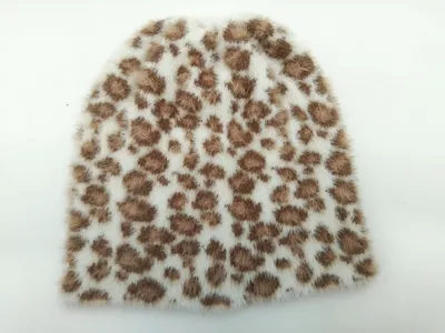 Weiche weiß-braune Kunstfell-Mütze mit Leopardenmuster, flach auf hellem Untergrund fotografiert
