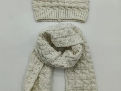 Creme-weißes Zopfmuster-Strickset bestehend aus Wintermütze und langem passenden Schal, Draufsicht auf hellem Hintergrund