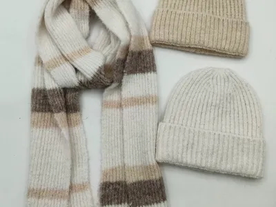 Zwei Rippenstrick-Beanies in Beige und Creme zusammen mit einem gemusterten Streifenstrickschal in Neutraltönen auf weißem Hintergrund