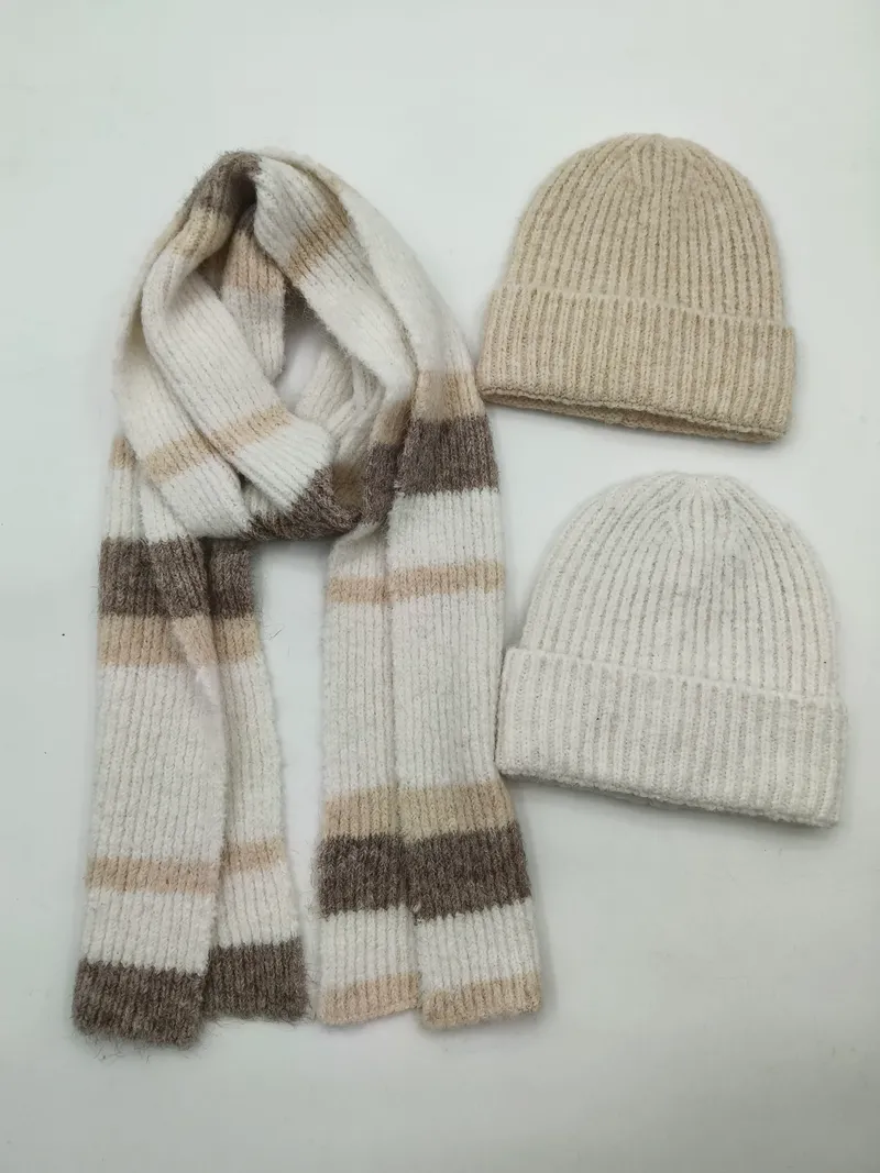 Zwei Rippenstrick-Beanies in Beige und Creme zusammen mit einem gemusterten Streifenstrickschal in Neutraltönen auf weißem Hintergrund