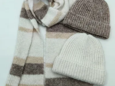 Draufsicht auf einen gemusterten Streifenstrickschal in Creme, Beige und Taupe mit zwei gerippten Wollmützen in Grau und Elfenbein