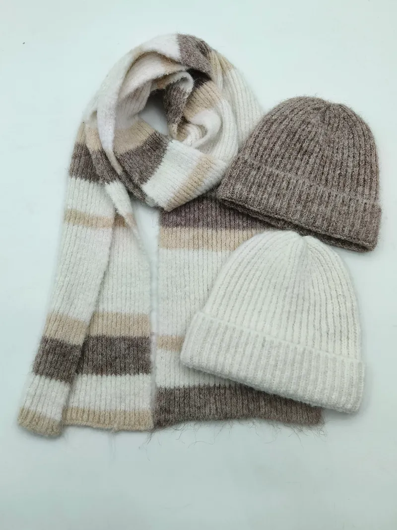 Draufsicht auf einen gemusterten Streifenstrickschal in Creme, Beige und Taupe mit zwei gerippten Wollmützen in Grau und Elfenbein