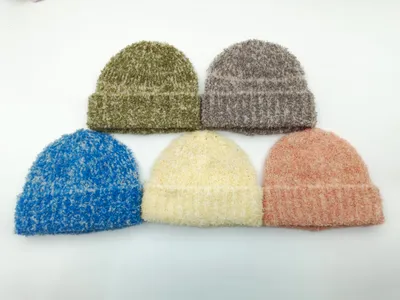 Fünf flauschige Bouclé-Strickmützen in Olivgrün, Grau, Blau, Creme und Altrosa auf weißem Hintergrund