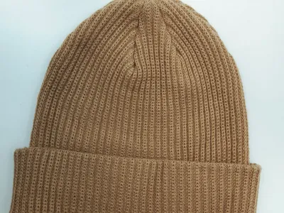Warme Beige-Braun Strickmütze mit Rippenoptik und breitem Umschlagkrempe, flach fotografiert auf weißem Grund