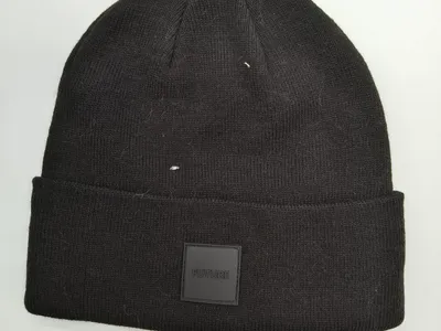 Schwarze Strickmütze mit breitem Aufschlag und quadratischem FUTURE Gummipatch-Logo auf weißem Hintergrund