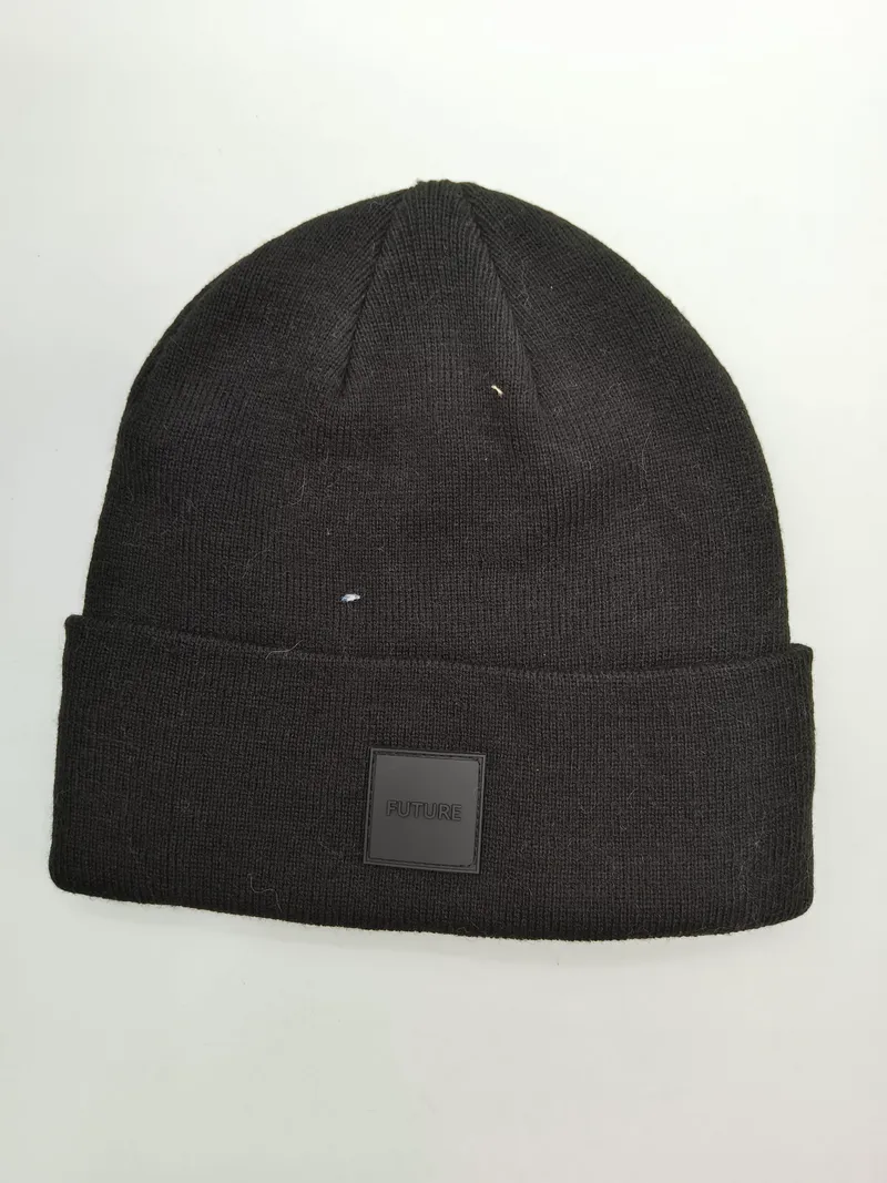Schwarze Strickmütze mit breitem Aufschlag und quadratischem FUTURE Gummipatch-Logo auf weißem Hintergrund