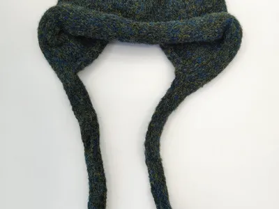 Strukturreiche Wintermütze mit Ohrenklappen in blau-grünem Melange aus Wollmischung mit langen Bindebändern, auf weißem Untergrund