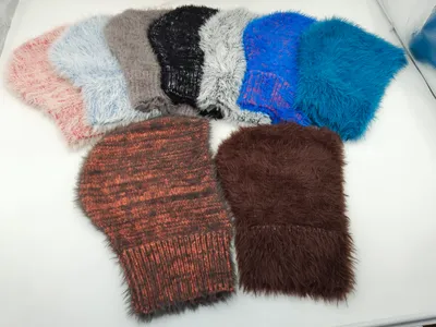 Sieben flauschige Wintermützen aus Kunstfell und Grobstrick in Pink, Grau, Schwarz, Weiß, Blau, Rostrot und Braun auf hellem Untergrund