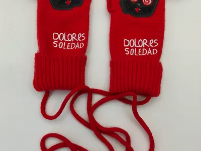 Rote gestrickte Handschuhe mit schwarzem Flausch-Monster-Motiv, Spiralaugen und langer Verbindungsschnur auf weißem Hintergrund