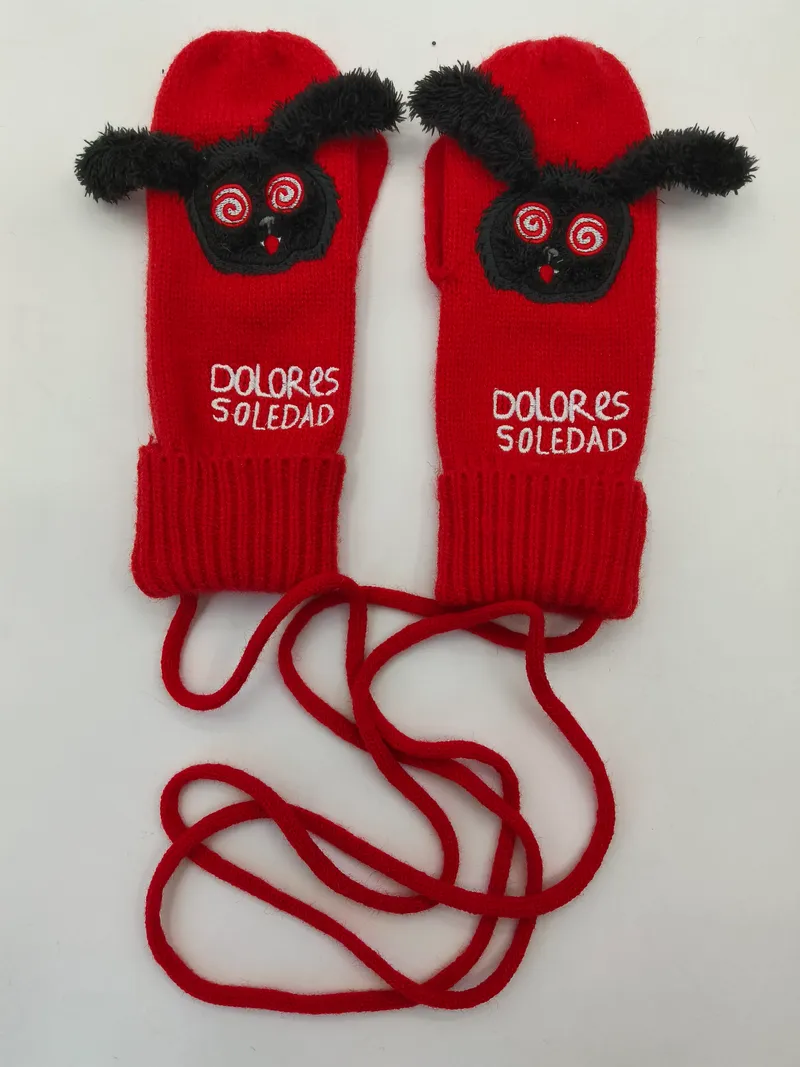Rote gestrickte Handschuhe mit schwarzem Flausch-Monster-Motiv, Spiralaugen und langer Verbindungsschnur auf weißem Hintergrund