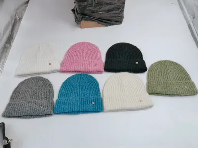Sieben Rippenstrick-Mützen in Weiß, Pink, Dunkelgrün, Salbeigrün, Grau, Blau und Creme auf weißem Untergrund