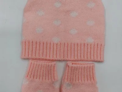 Rosa gestricktes Baby-Set bestehend aus Mütze mit Katzenohren und weißem Herzmuster sowie passenden Fäustlingen auf weißem Hintergrund