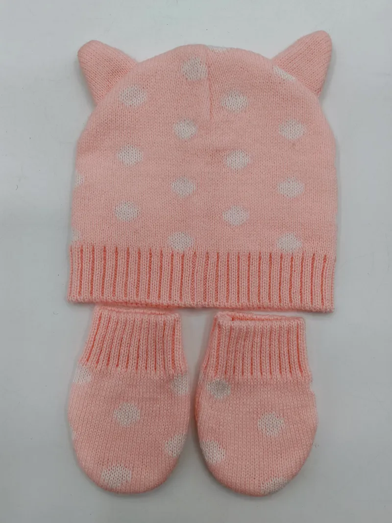 Rosa gestricktes Baby-Set bestehend aus Mütze mit Katzenohren und weißem Herzmuster sowie passenden Fäustlingen auf weißem Hintergrund