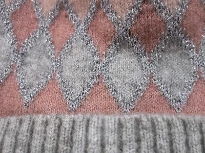 Detailaufnahme einer Strickmütze mit rosa-grauem Rautenmuster, silbernen Metallic-Fäden und geripptem grauem Bund