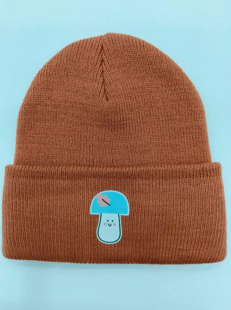 Rostbraune Rippenstrick-Umschlagmütze mit kawaii Pilzfigur als Aufnäher auf der Krempe, flach fotografiert