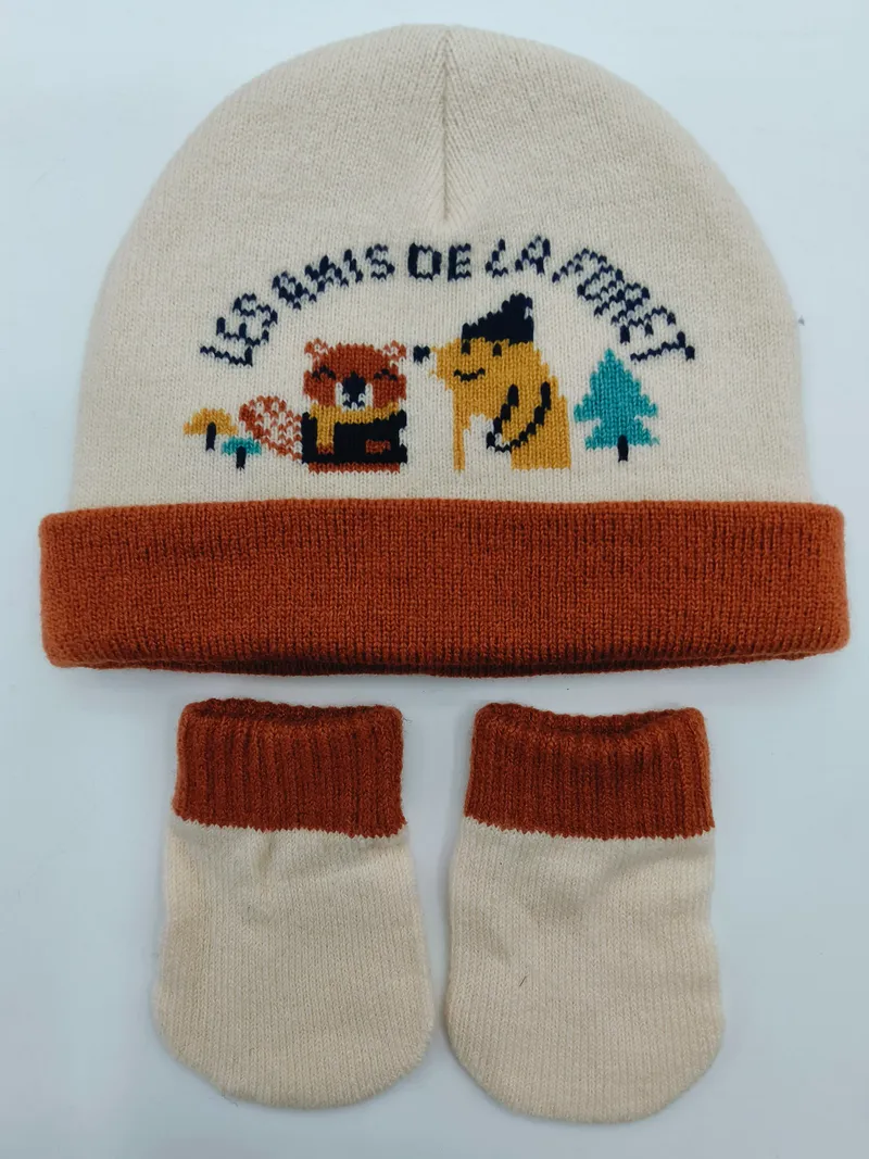 Creme und rostfarbenes Baby-Strickset aus Mütze mit Intarsia-Waldtiermotiven und passenden Babyschuhen, flach auf hellem Hintergrund