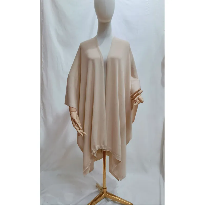 Beigefarbener, oversized Strickponcho mit offenem Vorderteil und geripptem Abschluss, drapiert auf einer Schneiderpuppe in neutralem Ton